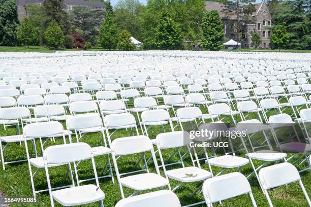 Rows of white folding chairs on green lawn.