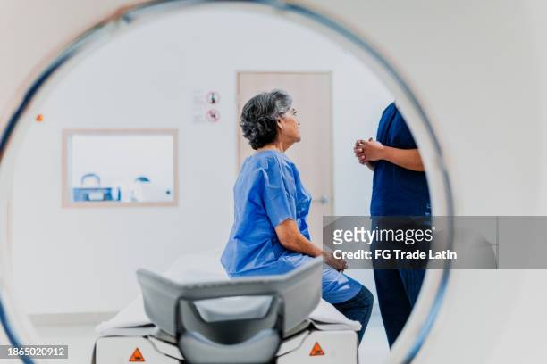 senior woman talking to a nurse on a mri tomography at hospital - mri machine stockfoto's en -beelden
