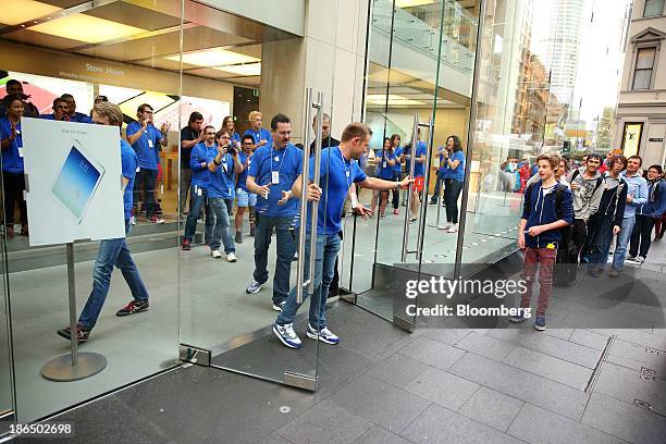 An Apple Inc. Employee opens the doors to customers who are waiting in line outside the company's George Street store ahead of the launch of the...