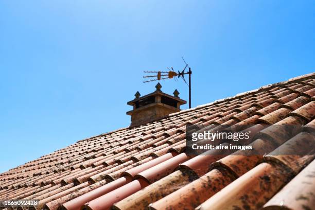 a roof covered with red tiles with a chimney on top and an antenna in the background overlooking the blue sky. - fernsehantenne stock-fotos und bilder