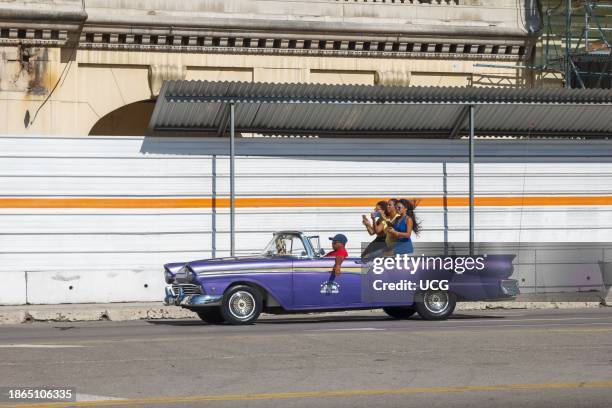 Havana, Cuba, Tourist women ride on a vintage American convertible car in the capital city. In the background, an old building is in reconstruction...