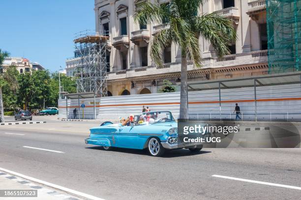 Havana, Cuba, A classic American convertible car drives by an old building undergoing revitalization or reconstruction in the downtown district.