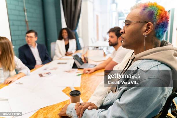 side portrait of mixed race artistic man sit on wheelchair at working meeting - mixed race young creatives in meeting stock-fotos und bilder