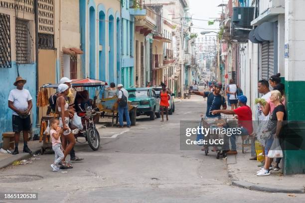 Havana, Cuba, A Cuban man sells food items with a small cart in a city corner. The urban lifestyle of other people is shown in the street scene.