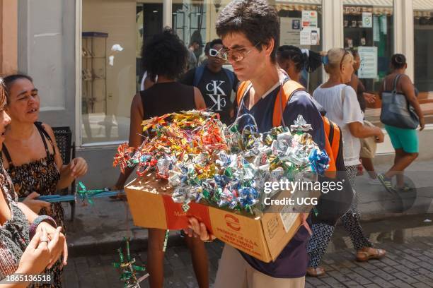 Havana, Cuba, A young, self employed Cuban man sells souvenirs made of aluminum cans on a city street. Other people and their real lifestyle are seen...