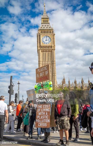 Lone environmental anti-plastic protester stands outside Big Ben and the Houses of Parliament in Westminster, London, UK, holding placards and waste...