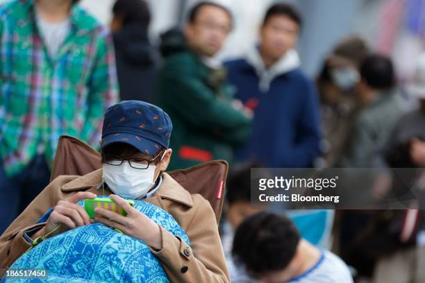 Customer uses a mobile device as he waits in line outside an Apple Inc. Store ahead of the launch of the company's iPad Air in the Ginza district of...