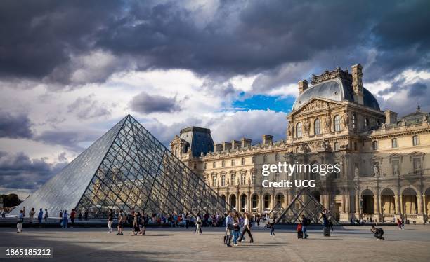 Tourists in Napoleon Courtyard next to the glass Louvre Pyramid and Louvre Museum, Paris, France.