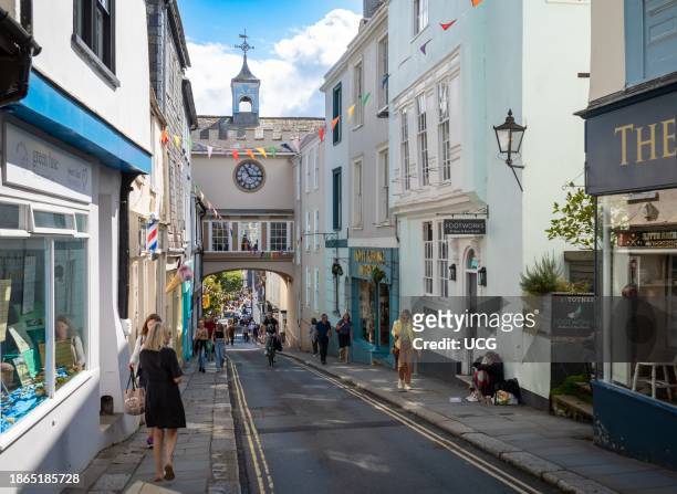 People walk near the 14th century East Gate Arch with its large clock positioned over the High Street in Totnes, Devon, UK.