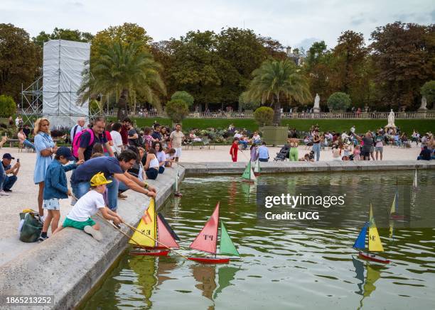 Father plays with his children as they launch model sailing boats on the pond in the heart of the popular Jardin du Luxembourg in Paris, France.