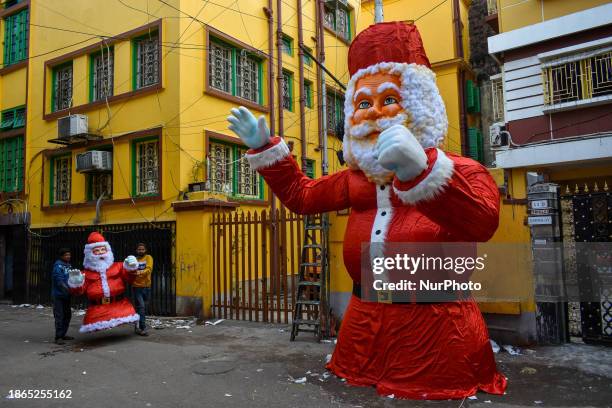 Workers are carrying a Styrofoam figure of Santa Claus in front of a giant figurine of Santa, which is being made as part of Christmas decorations,...