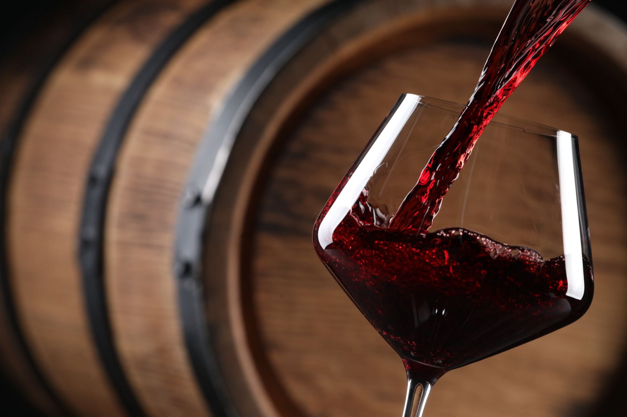 Pouring red wine into glass near wooden barrel, closeup. Space for text Pouring red wine into glass near wooden barrel, closeup. Space for text