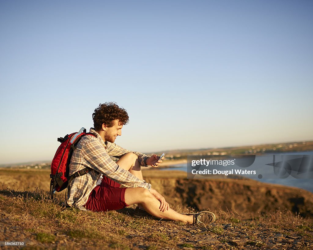 Male hiker using mobile phone on UK coastline.