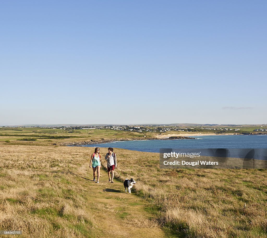 Hikers walking along coastal path with dog.