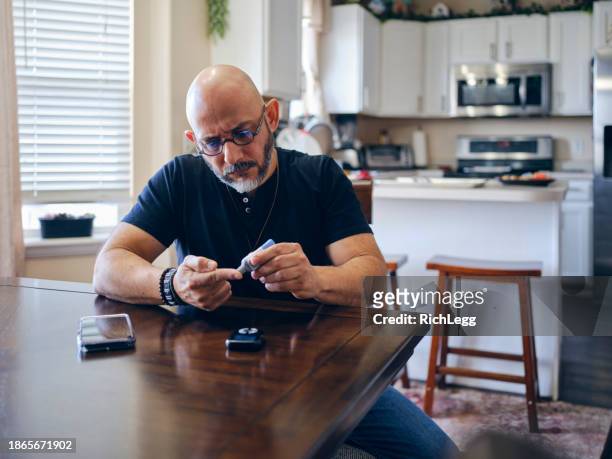 a mature man in a home checking his blood sugar - blood sugar test stock pictures, royalty-free photos & images
