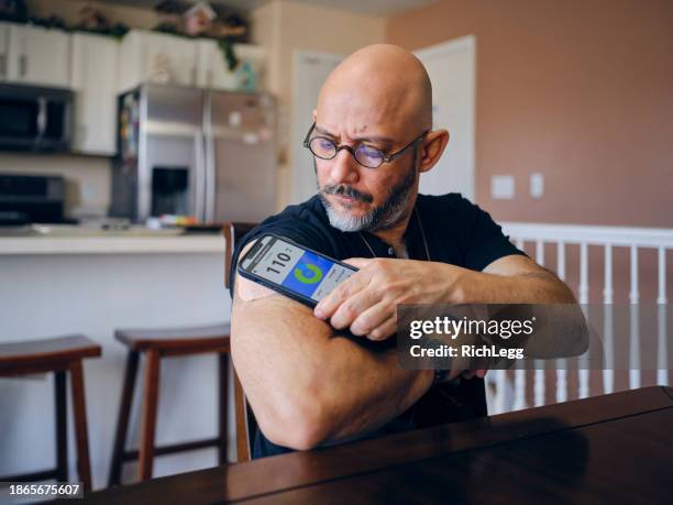 a mature man in a home checking his blood sugar - diabetes technology stock pictures, royalty-free photos & images