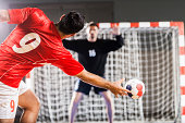 Handball player in red shooting toward a net