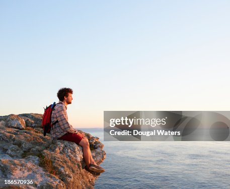Hiker sitting on coastal rock looking out to sea. Hiker sitting on coastal rock looking out to sea.