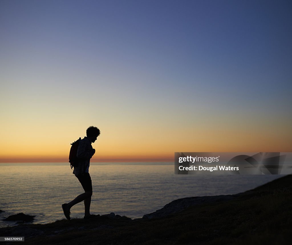 Hiker walking along coastline at sunset.