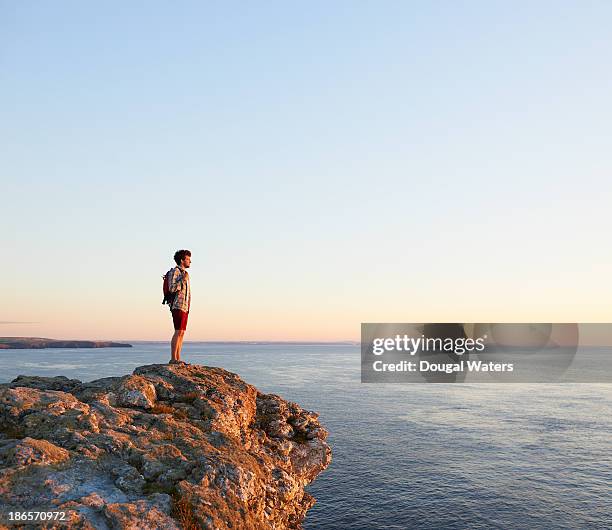 hiker standing on rock and looking out to sea. - sea cliff stock pictures, royalty-free photos & images