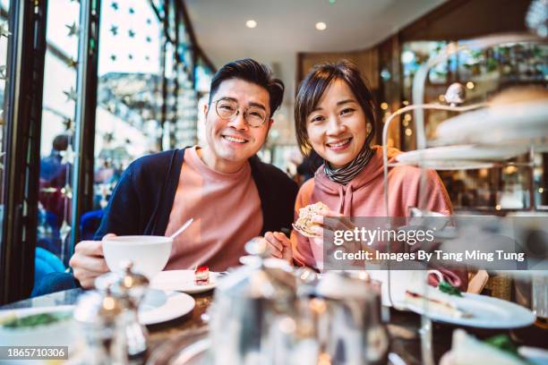 happy asian couple smiling joyfully at the camera while enjoying traditional afternoon tea in restaurant - tea shop stock pictures, royalty-free photos & images