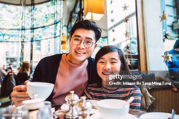 dad & daughter smiling joyfully at the camera while enjoying traditional afternoon tea in restaurant - englische tea time stock-fotos und bilder