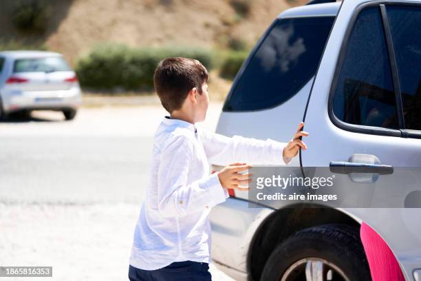 side view of a well-dressed boy opening the doors of a car standing alone on a sunny day - boy skirt stock pictures, royalty-free photos & images