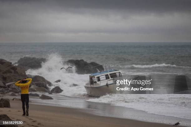 Lifeguard observes a boat that was sent into the rocks on Deer Creek beach after heavy winds during a storm on December 21, 2023 in Oxnard,...