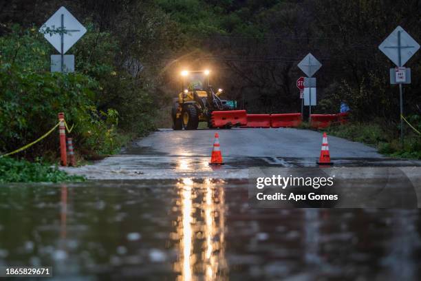 City workers close a road after a creek overflows during heavy rains in Zuma Beach during heavy rains on December 21, 2023 in Malibu, California....