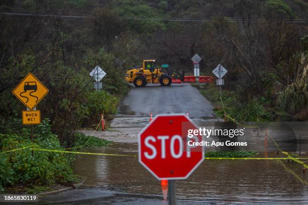 City workers close a road after a creek overflows during heavy rains in Zuma Beach during heavy rains on December 21, 2023 in Malibu, California....