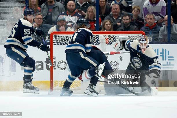 Elvis Merzlikins of the Columbus Blue Jackets scrambles after the loose puck as Kent Johnson checks Tom Wilson of the Washington Capitals into the...