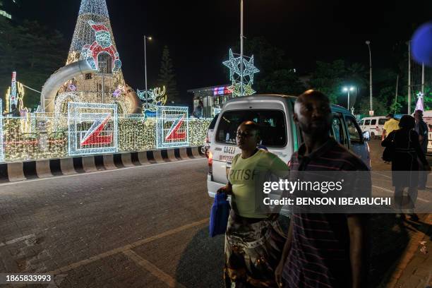 Commuters walk next to some Christmas decorations on the streets of Victoria Island in Lagos on December 18, 2023. Christmas and year-end...