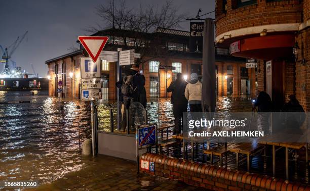 People observe the rising water around the fishmarket and surrounding streets on the Hamburg waterfront being flooded due to a storm surge caused by...