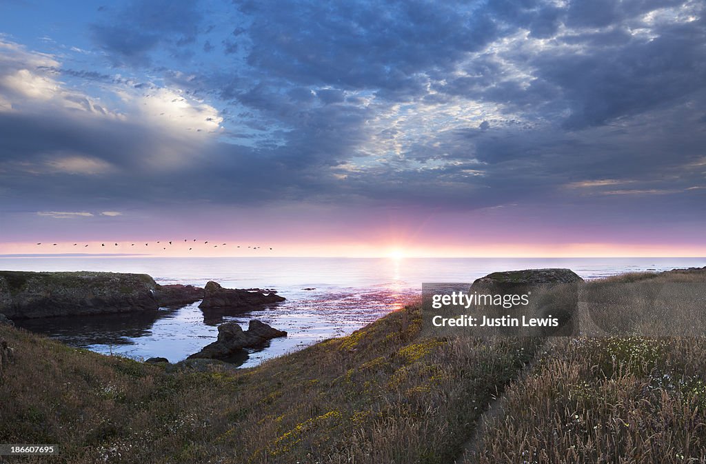 Sunset over rocky ocean coastline with trail