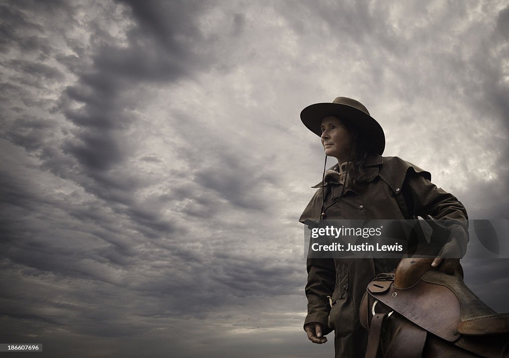 Woman with horse saddle and hat & stormy sky