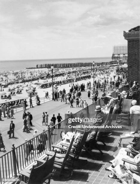 People sitting on a balcony overlooking the boardwalk on warm summer day, Atlantic City, New Jersey, mid to late 1920s.
