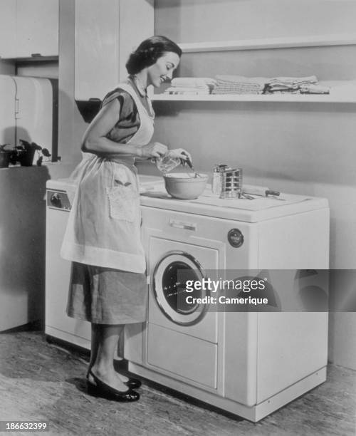 Woman with apron standing in front of a washing machine, 1960.