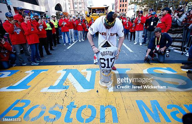 Jonny Gomes of the Boston Red Sox lays the World Series trophy and the 'Boston Strong 617' jersey onto the finish line of the Boston Marathon on...