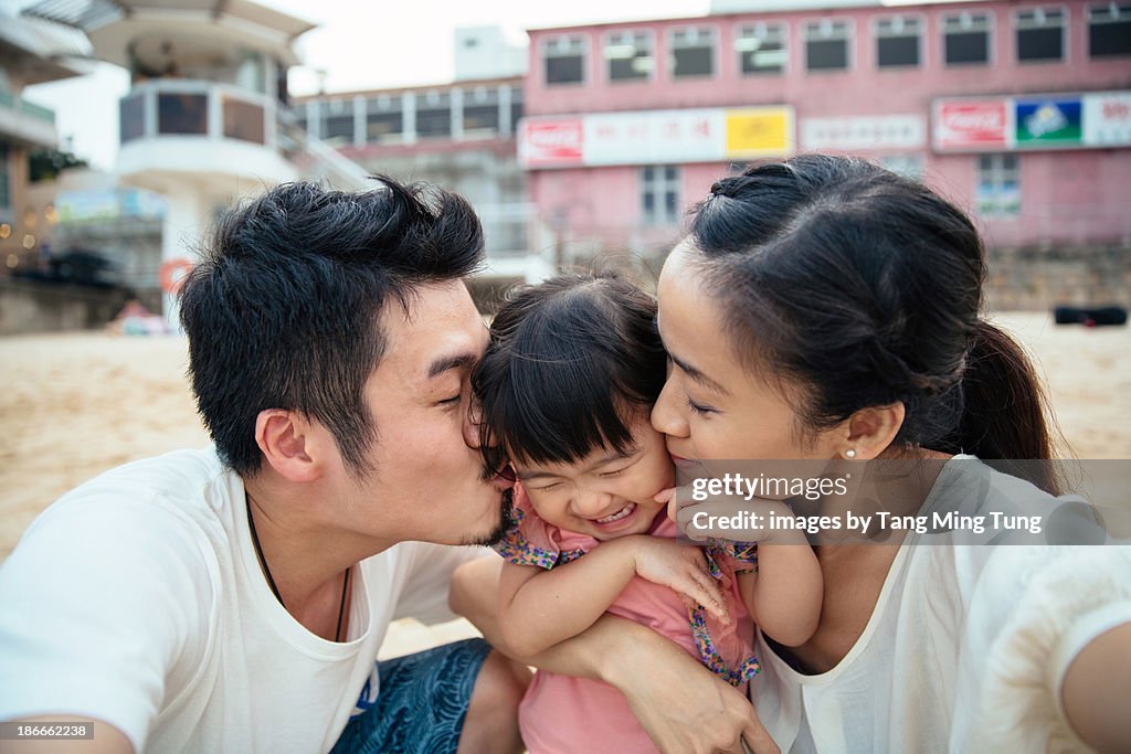 Mom & dad kissing lovely toddler girl's cheek