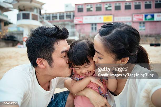 Mom & dad kissing lovely toddler girl's cheek
