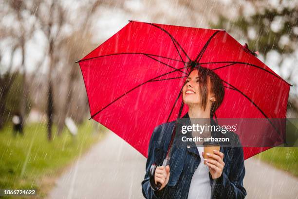 young woman with a red umbrella drinking coffee on the go in the park - umbrella rain stock pictures, royalty-free photos & images