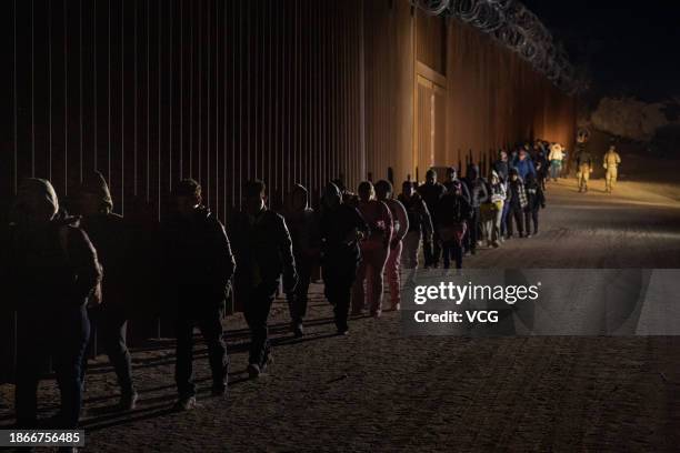 Asylum-seeking migrants walk along the US-Mexico border fence near the Jacumba Hot Springs on December 18, 2023 in San Diego, California.