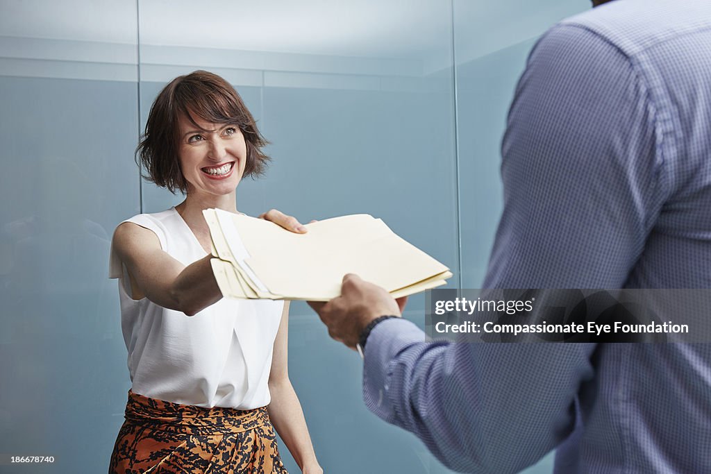 Woman handing man with documents in office