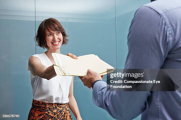 woman handing man with documents in office - pasar fotografías e imágenes de stock