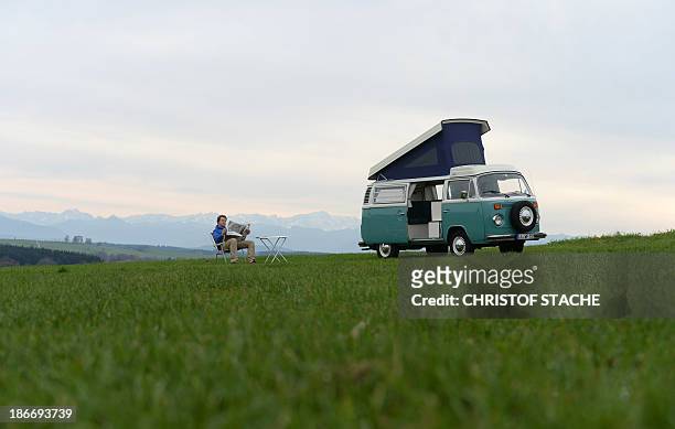 Volkswagen Kombi owner Wanja Fuhrmann sits on a camping chair and reads a newspaper next to his Volkswagen T2 camper van built in the year 1975 near...