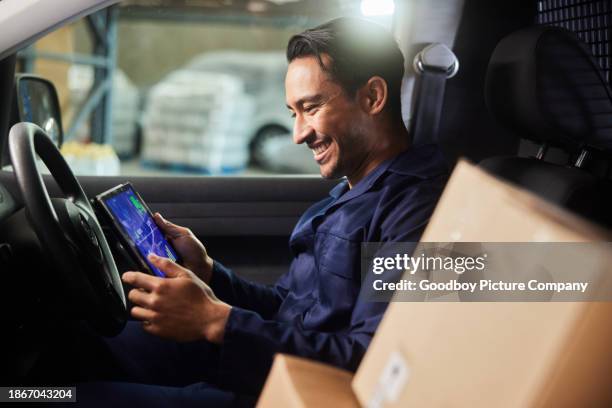 smiling delivery person using a tablet while sitting in his van in a warehouse - inside a van stock pictures, royalty-free photos & images