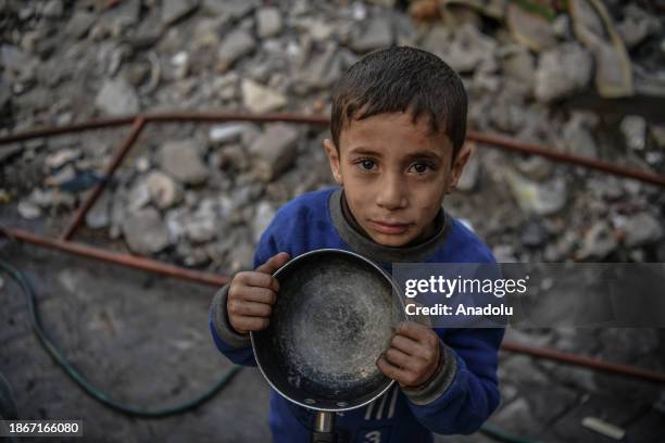 Palestinian child, holding empty pot, wait to receive food distributed by volunteers for Palestinian families ,displaced to Southern Gaza due to...