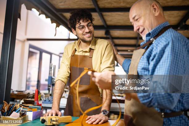orgulloso sastre senior que comparte sus conocimientos y experiencia con su hijo, un aprendiz - cinturón de cuero fotografías e imágenes de stock