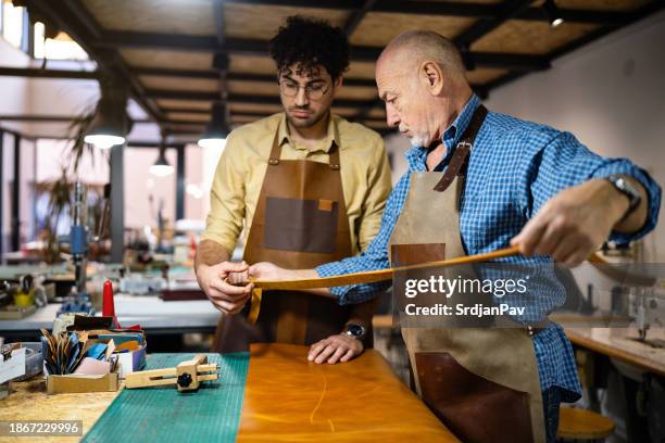 senior caucasian male tailor and young male trainee working together at the leather workshop - leather belt stock pictures, royalty-free photos & images