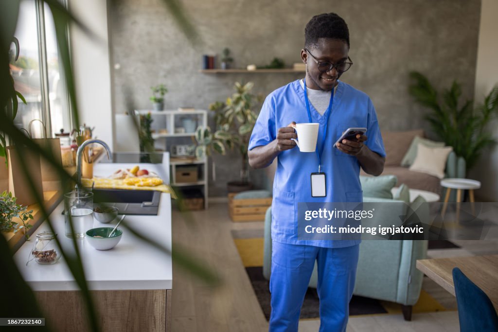 Young man wearing medical scrubs using his phone at home
